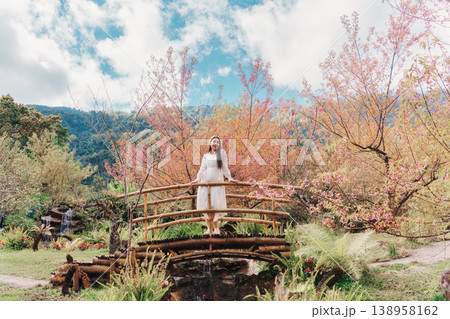 Relaxed woman standing on wooden bridge in Wild Himalayan Cherry blooming Relaxed woman standing on wooden bridge in Wild Himalayan Cherry blooming 138958162