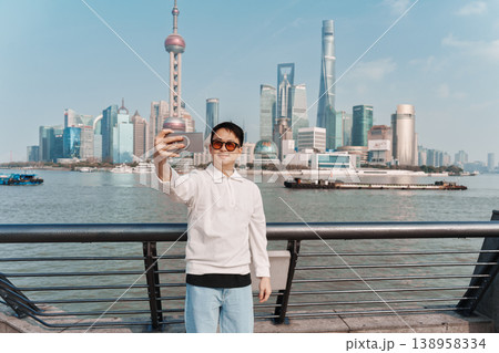 Happy man taking selfie by smartphone with Oriental Pearl Tower and iconic skyscraper in Lujiazui business center at The Bund 138958334