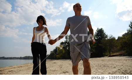 Romantic couple holding hands of each other and jogging at coastal. Happy pair running along seashore at sunny day. Lovers spending time together at resort. Concept of summer vacation or holiday 138958543
