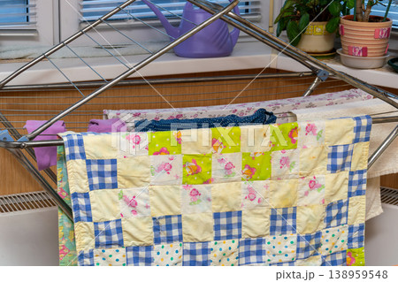 Colorful Patchwork Quilt Hanging on Indoor Drying Rack with Laundry and Potted Plants in Home 138959548