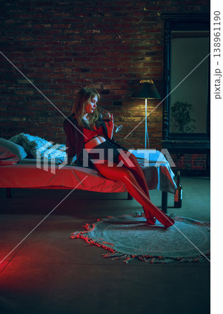 Young woman in red lingerie drinking wine sitting on bed in moody loft interior. 138961190