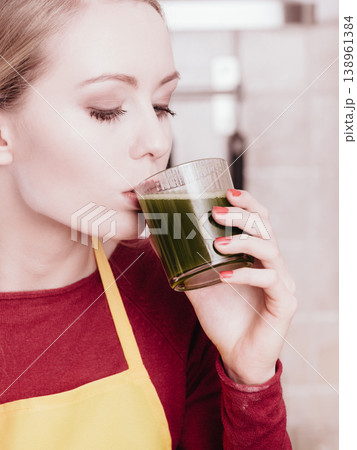 Woman in kitchen holding vegetable smoothie juice Woman in kitchen holding vegetable smoothie juice 138961384