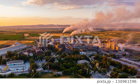 Industrial cement plant with smokestacks and agricultural fields at sunset 138961596
