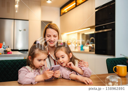 Mother and twin daughters sharing smartphone in kitchen 138962891