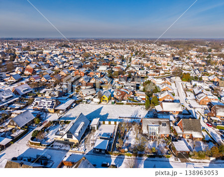 Aerial view of a picturesque European residential neighborhood covered in white snow. Sunny winter day showing rooftops with solar panels, gardens, and streets in a peaceful suburban community. 138963053