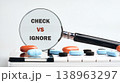 Magnified colorful pills and CHECK VS IGNORE illustrate a critical health choice 138963297