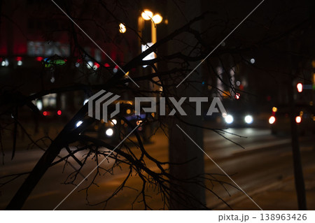 Dark urban street scene with blurred car lights and tree branch silhouettes, creating a moody nighttime atmosphere. Dark urban street scene with blurred car lights and tree branch silhouettes, creating a moody nighttime atmosphere. 138963426