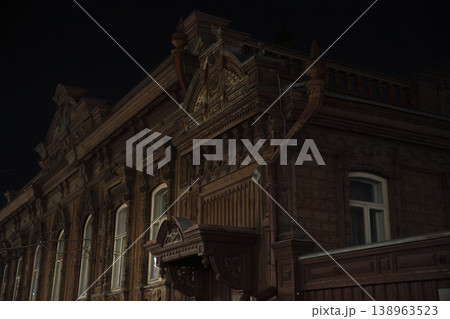 Ornate historic wooden building facade illuminated by warm light at night, highlighting intricate architectural details and creating a moody atmospheric scene. 138963523