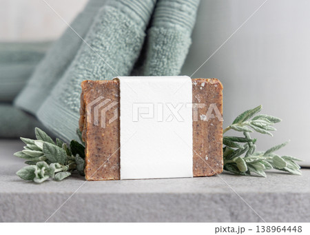 Brown solid soap bar with blank paper label mockup near with leaves and sage green bath towel 138964448