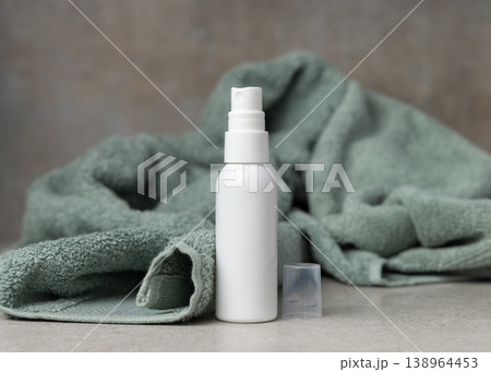 White spray cosmetic bottle mockup near sage green bath towel on stone. Unbranded blank packaging White spray cosmetic bottle mockup near sage green bath towel on stone. Unbranded blank packaging 138964453