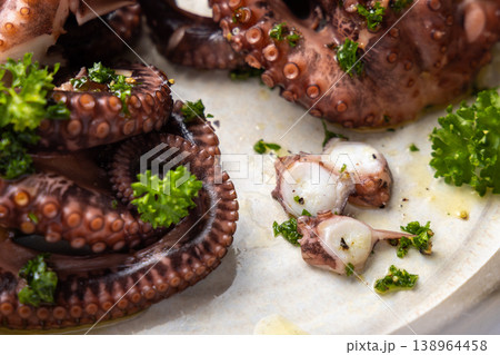 Boiled octopus tentacles and sliced pieces on ceramic plate top view. Olive oil and parsley dressing Boiled octopus tentacles and sliced pieces on ceramic plate top view. Olive oil and parsley dressing 138964458