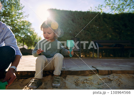 Toddler Playing With Sand Toy in Sunlit Park With Parent Nearby 138964566