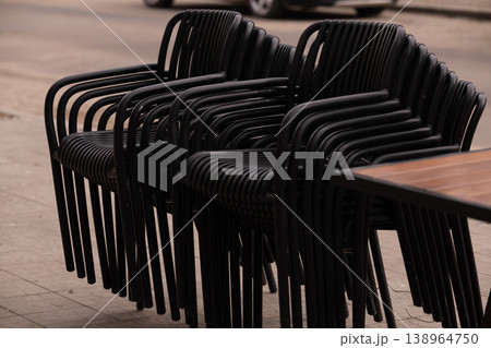 Row of Black Plastic Chairs Stacked Outdoors Near Wooden Table in Urban Setting Row of Black Plastic Chairs Stacked Outdoors Near Wooden Table in Urban Setting 138964750