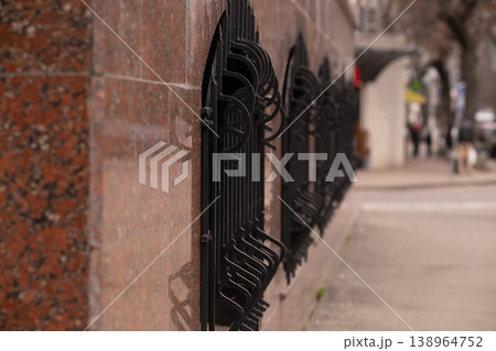 Black Wrought Iron Fence Against Polished Red Granite Stone Wall in Urban City Street Black Wrought Iron Fence Against Polished Red Granite Stone Wall in Urban City Street 138964752