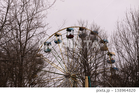 Vintage Ferris Wheel with Colorful Passenger Gondolas Peeking Through Bare Winter Tree Branches Vintage Ferris Wheel with Colorful Passenger Gondolas Peeking Through Bare Winter Tree Branches 138964820
