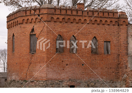 Old Red Brick Tower with Gothic Arched Windows and Large Structural Crack under Overcast Sky 138964829