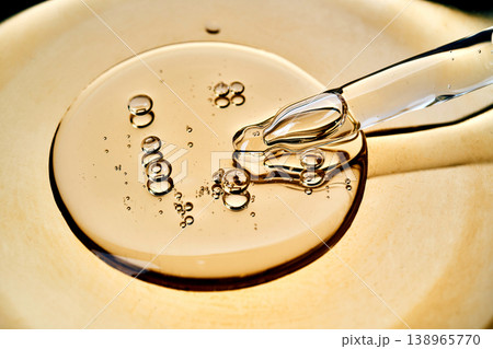 Golden cosmetic serum dripping from glass pipette 138965770