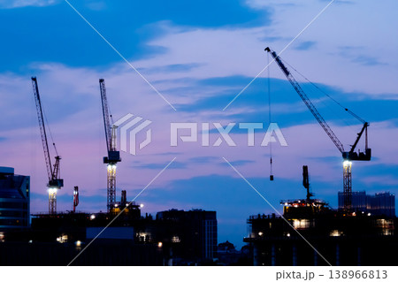 Tower cranes silhouettes and unfinished building construction against night sky Tower cranes silhouettes and unfinished building construction against night sky 138966813