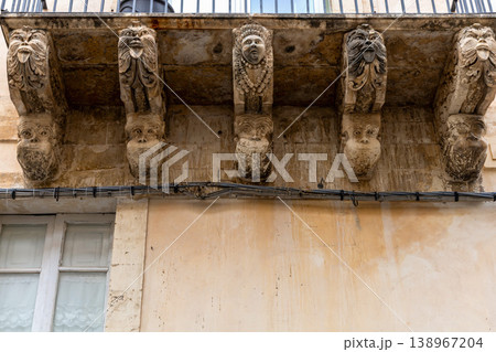 Carved stone mascarons supporting a baroque balcony on a historic building facade in the town of Noto, Sicily, Italy Carved stone mascarons supporting a baroque balcony on a historic building facade in the town of Noto, Sicily, Italy 138967204