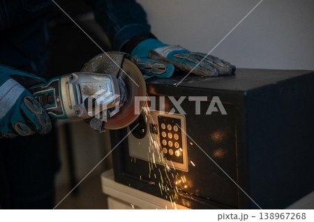 A man breaks into a safe with a grinder. 138967268