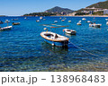 Small fishing boat anchored in crystal clear turquoise water near Adriatic coast with mountains and coastal town in background, sunny summer day, calm sea and travel vibe 138968483