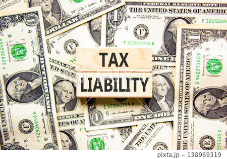 Tax liability words symbol. Concept words Tax liability on beautiful wooden blocks. Beautiful dollar bills background. Dollar bills. Business and Tax liability words concept. Copy space. 138969319