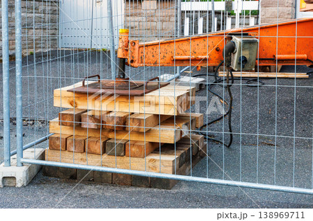 Stacked wooden cribbing supporting crane outrigger behind safety fence. Heavy equipment support and stability setup. 138969711