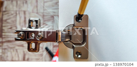 Marking the position of the screw hole on a furniture hinge with a pen Marking the position of the screw hole on a furniture hinge with a pen 138970104