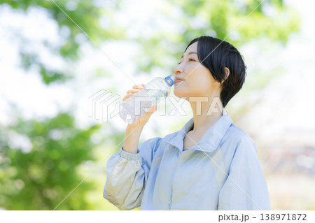 新緑の屋外で水分補給をする女性の横顔ポートレート　運動やスポーツの間にペットボトルの水を飲む 138971872