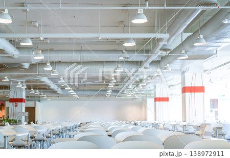 Empty white chair and table in shopping mall cafeteria with visible ceiling ventilation system, air ducts, pipes and fire sprinkler infrastructure, modern interior architecture. Public dining space. Empty white chair and table in shopping mall cafeteria with visible ceiling ventilation system, air ducts, pipes and fire sprinkler infrastructure, modern interior architecture. Public dining space. 138972911