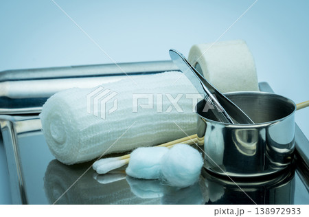 Wound care dressing set on stainless steel plate. Cotton ball with alcohol, cotton stick, surgical tape, forceps and conform bandage. Sterile medical supplies for treatment and infection prevention. 138972933