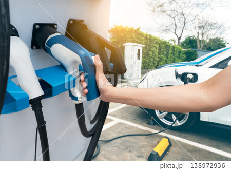 Hand holding electric plug-in charger on blur car charging. EV car charging at electric car charging station. EV car charging point. Electric vehicle fast charge. Sustainable power. Green energy. Hand holding electric plug-in charger on blur car charging. EV car charging at electric car charging station. EV car charging point. Electric vehicle fast charge. Sustainable power. Green energy. 138972936