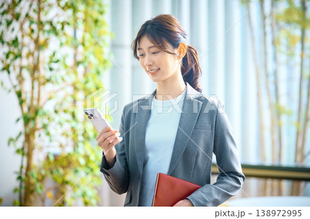 オフィスでスマートフォンを使いながら微笑む若手女性ビジネスパーソン オフィスでスマートフォンを使いながら微笑む若手女性ビジネスパーソン 138972995