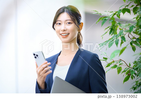笑顔でスマートフォンとノートパソコンを持つビジネスウェアの日本人女性 笑顔でスマートフォンとノートパソコンを持つビジネスウェアの日本人女性 138973002