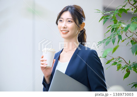 オフィスで笑顔を見せるビジネスウーマン ノートパソコンとコーヒーを持つ若い女性社員 オフィスで笑顔を見せるビジネスウーマン ノートパソコンとコーヒーを持つ若い女性社員 138973003