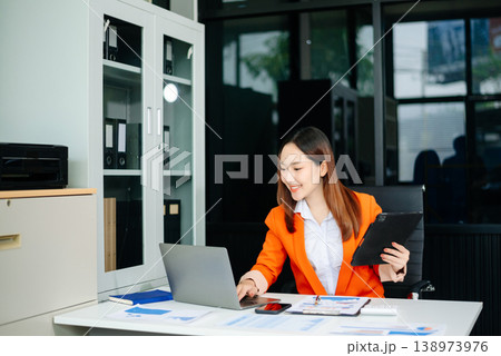 Young attractive Asian female office worker business suits smiling in office Young attractive Asian female office worker business suits smiling in office 138973976