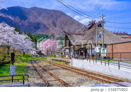雄大な山並みと満開の桜に彩られた茅葺きの宿場駅 湯野上温泉駅 138975902