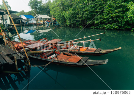 Traditional wooden boats and stilt houses along a calm canal surrounded by lush green mangrove forest. Traditional wooden boats and stilt houses along a calm canal surrounded by lush green mangrove forest. 138976063