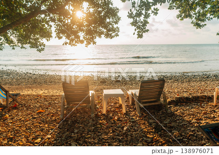 Relaxing Beach Chairs Under Tree Shade at Sunrise on a Pebbly Shore Relaxing Beach Chairs Under Tree Shade at Sunrise on a Pebbly Shore 138976071