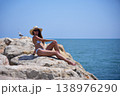 Woman enjoying sun on seaside rocks in bikini during summer day 138976290