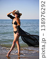 Woman walking in shallow sea water in black bikini with sheer cover up 138976292