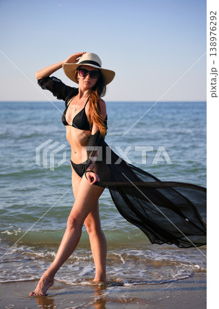 Woman walking in shallow sea water in black bikini with sheer cover up 138976292