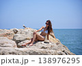Woman relaxing on coastal rocks with sun hat beside her by the sea 138976295