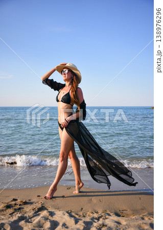 Woman walking on sandy beach in black bikini with flowing cover up 138976296