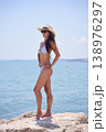 Woman standing in profile on seaside rocks in bikini and sun hat 138976297