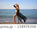 Woman posing at shoreline in black bikini with flowing sheer cover up 138976306