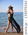 Woman walking on beach in black bikini with sheer cover up and sun hat 138976342