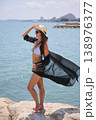 Woman in bikini and black cover up standing on rocks by the sea 138976377