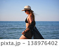 Side profile of woman on beach in black bikini with sheer cover up 138976402