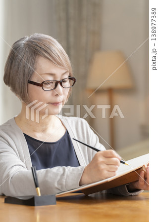 リビングでエンディングノートを書くシニア女性 リビングでエンディングノートを書くシニア女性 138977389